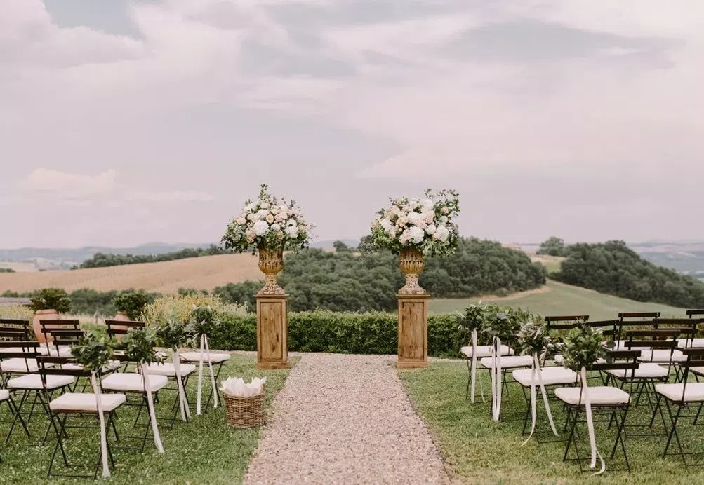 Chairs set up for an outdoor wedding ceremony in a countryside setting with white flowers tied to the chairs