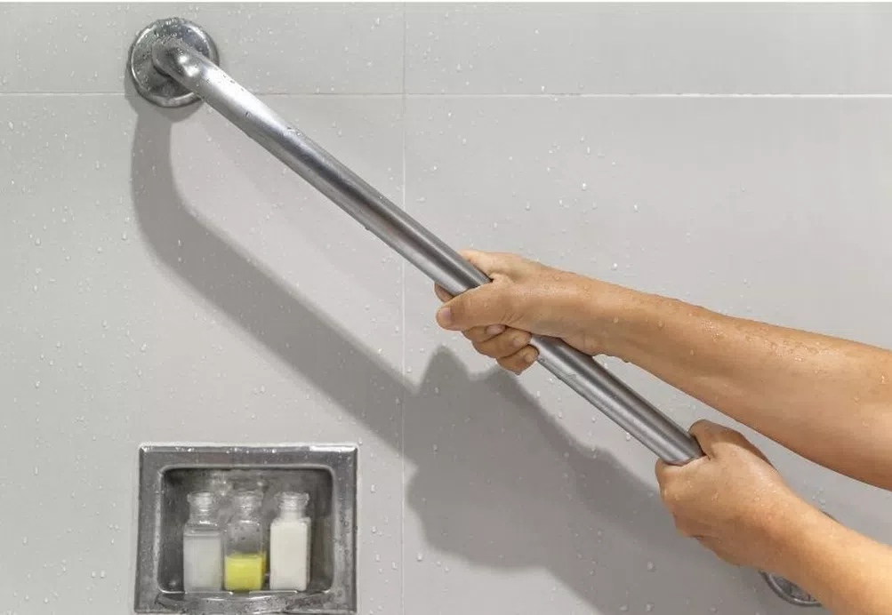 A person gripping a shower handrail for support while standing in a shower.
