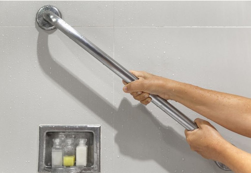 A person gripping a shower handrail for support while standing in a shower.
