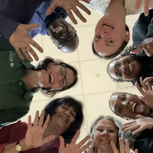 Laughter Yoga, photo of a group of people smiling and laughing, gathered in a circle and looking down into the camera