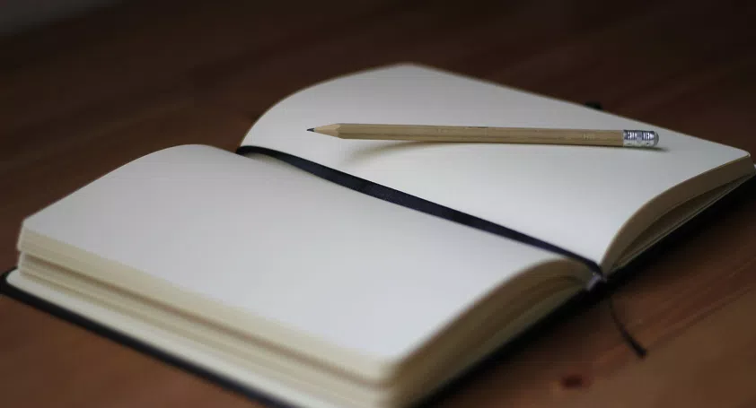 Image of a notebook open on an empty page with a pencil resting on top of it