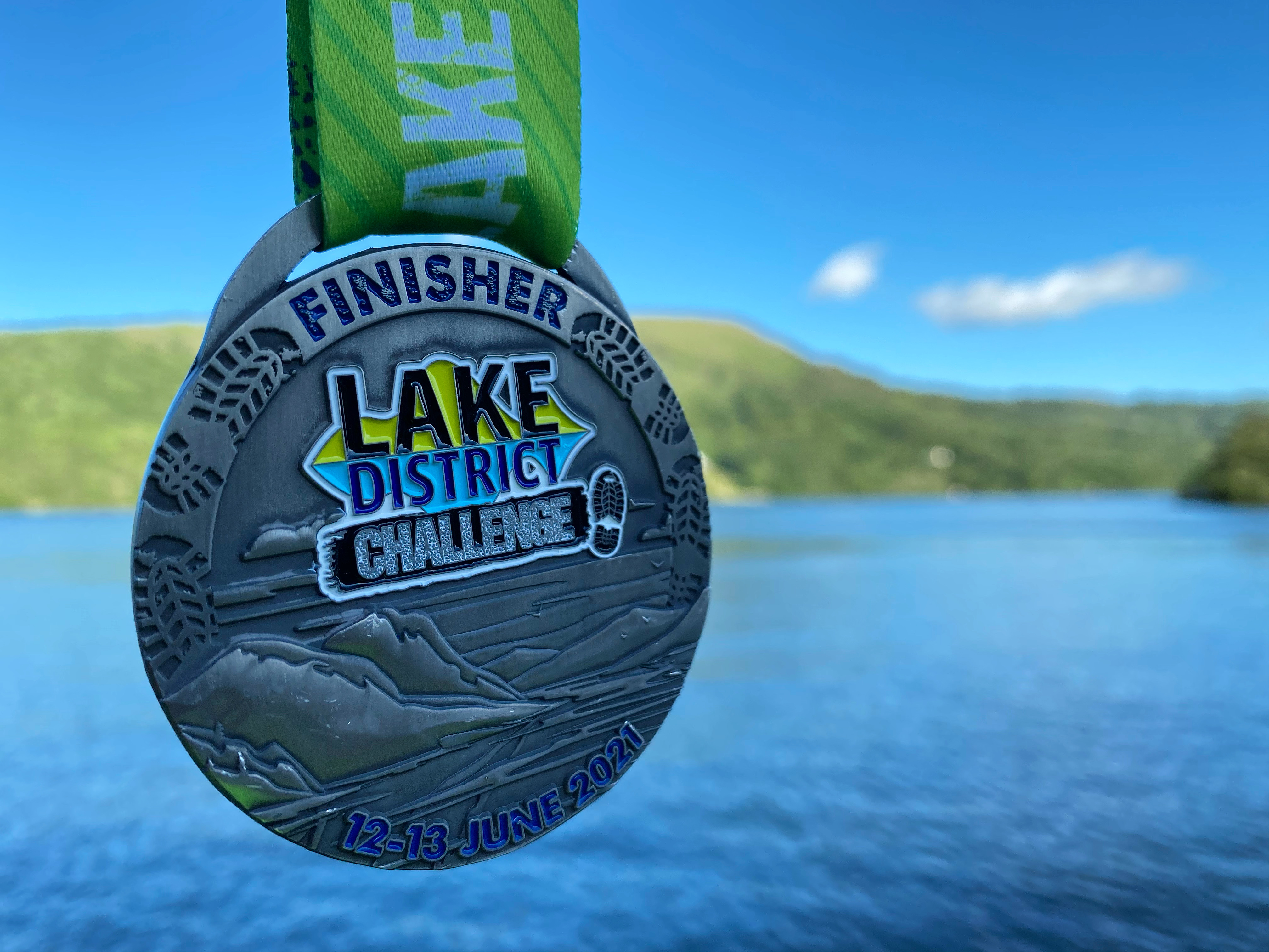 Lake District Ultra Challenge 2026, photo of finisher medal in the foreground with a lake in the background