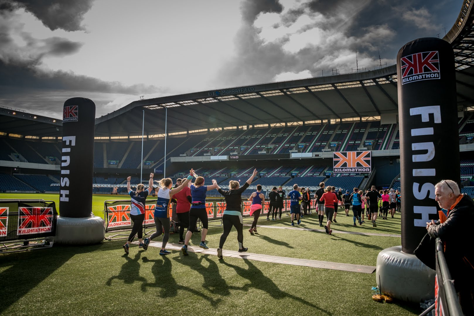 2026 Kilomathon Scotland, photo of event participants crossing the finish line as a group with their hands punching the air
