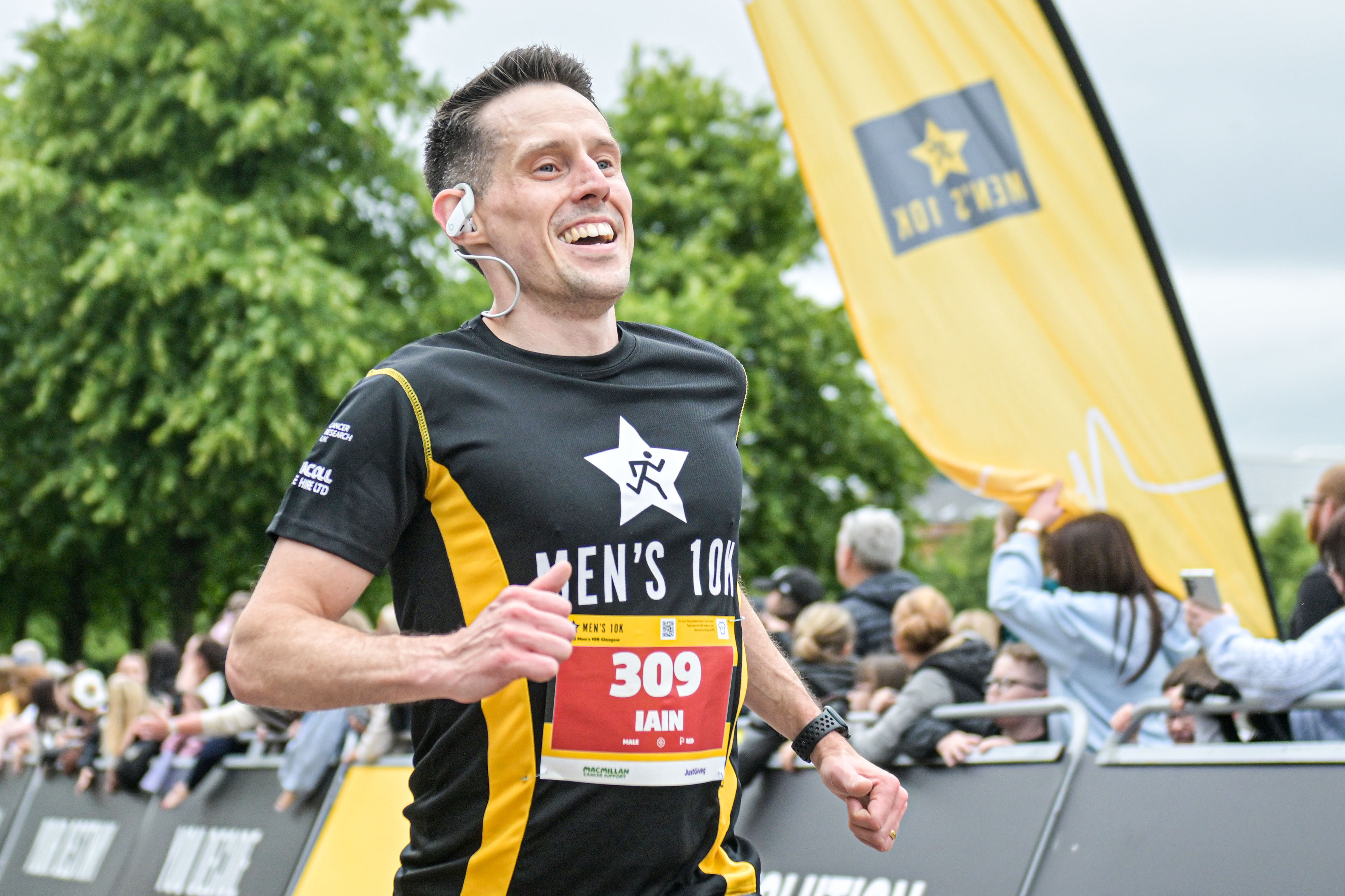 2026 Men’s 10K Glasgow, photo of event participant crossing the finish line with a smile on his face