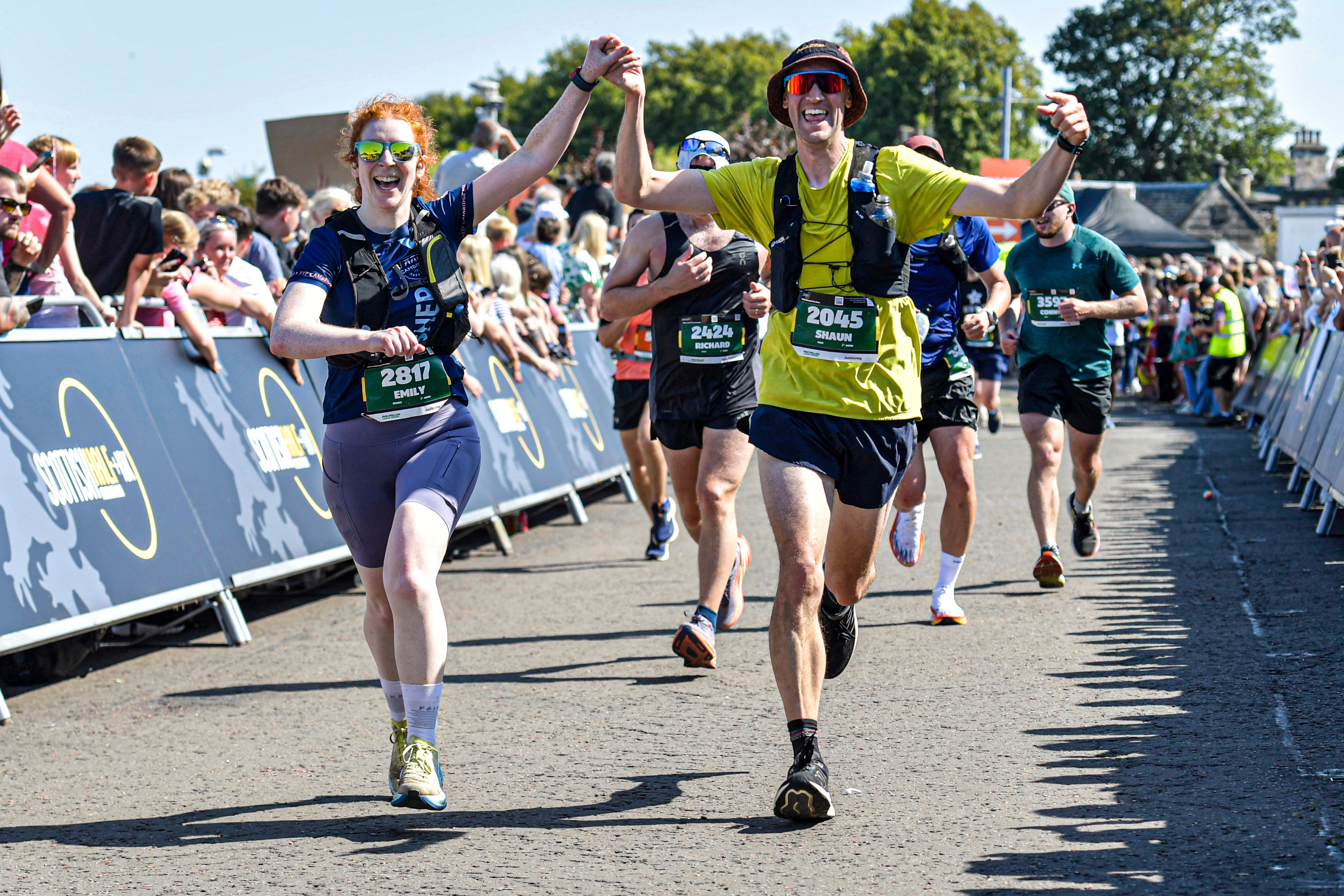 2026 Scottish Half Marathon, photo of two event participants smiling and holding hands as they run towards the finish line, which is just out of shot
