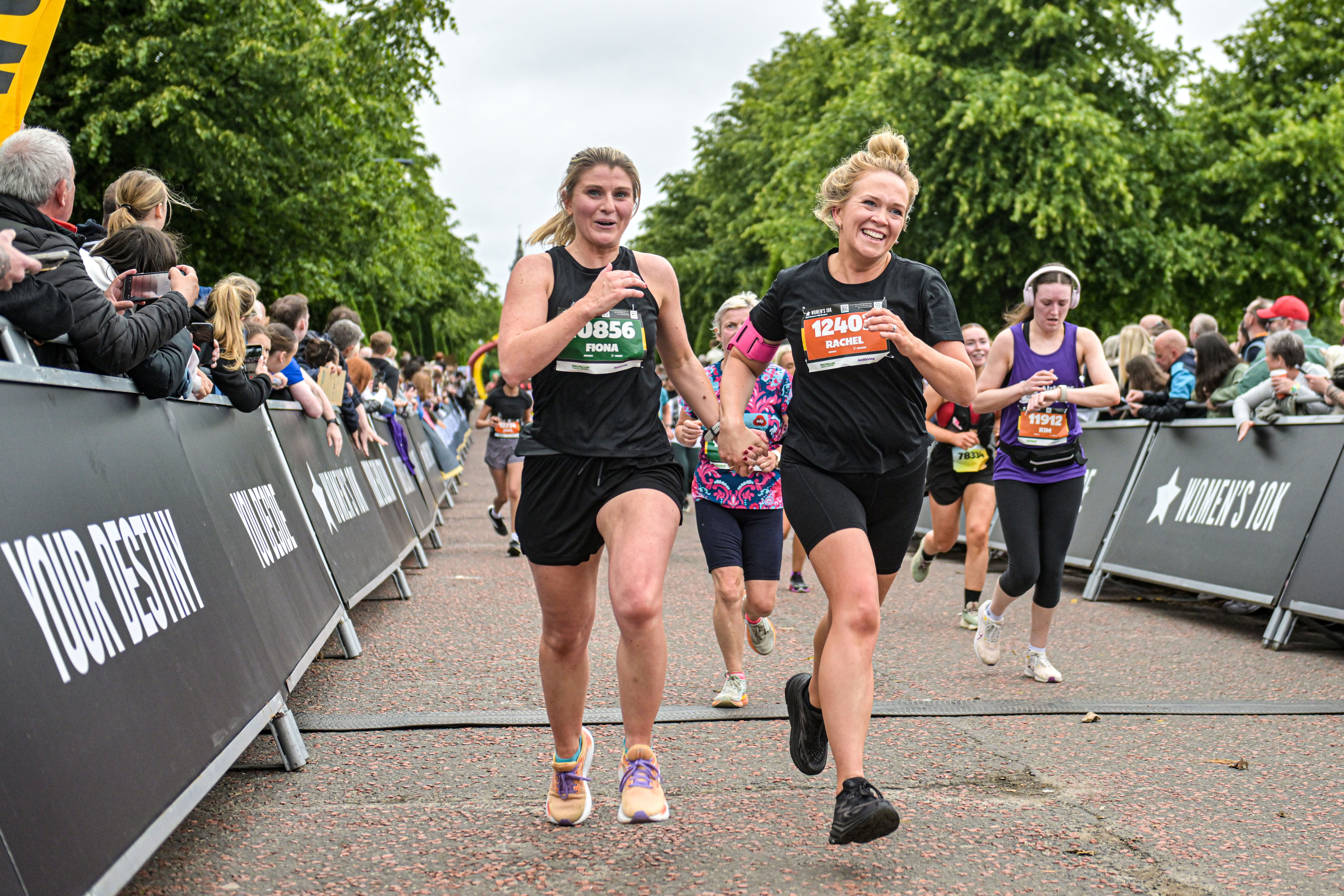 2026 Women’s 10K Glasgow, photo of two event participants smiling and holding hands as they run towards the finish line, which is just out of shot